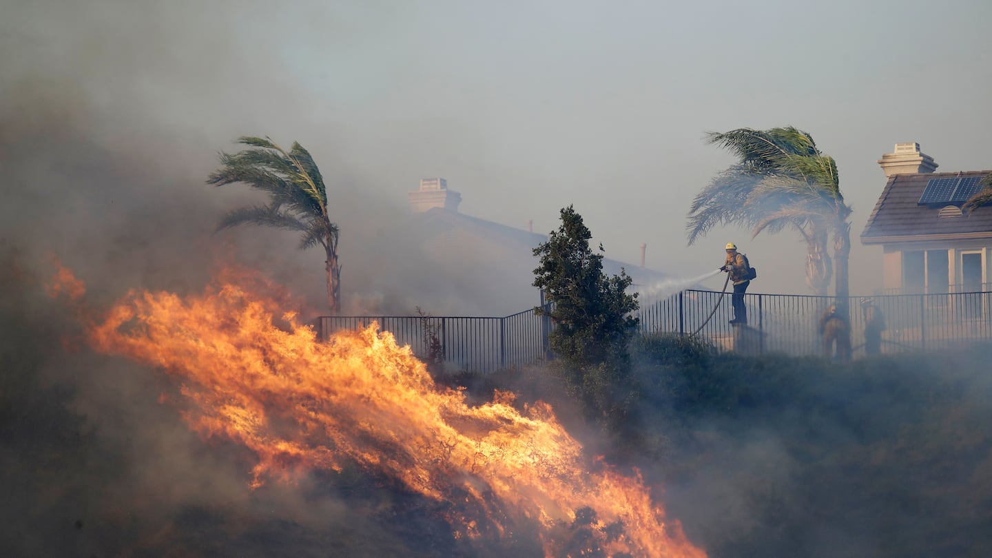 A firefighter sprays water in front of an advancing wildfire Friday, Oct. 11, 2019, in Porter Ranch, Calif.