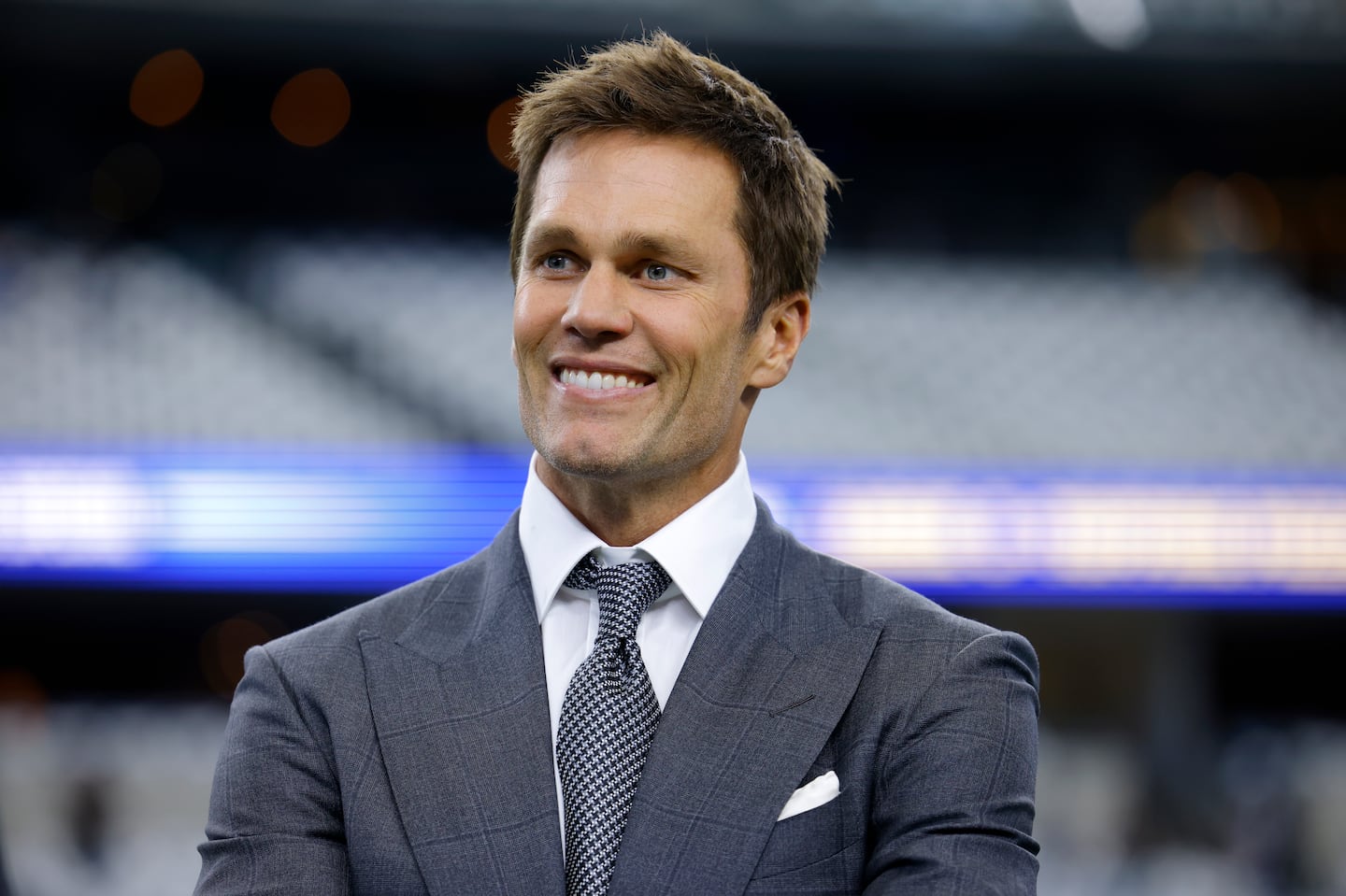 Fox Sports lead NFL analyst Tom Brady stands on the field during warmups before an NFL football game between the Detroit Lions and the Dallas Cowboys in Arlington, Texas, Sunday, Oct. 13, 2024.