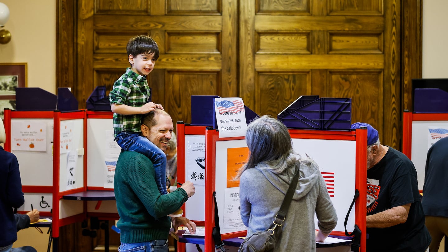 Asher Glass, 4, sits on the shoulders of his father Jason as his parents cast early ballots at Needham Town Hall for the Nov. 5 general election.