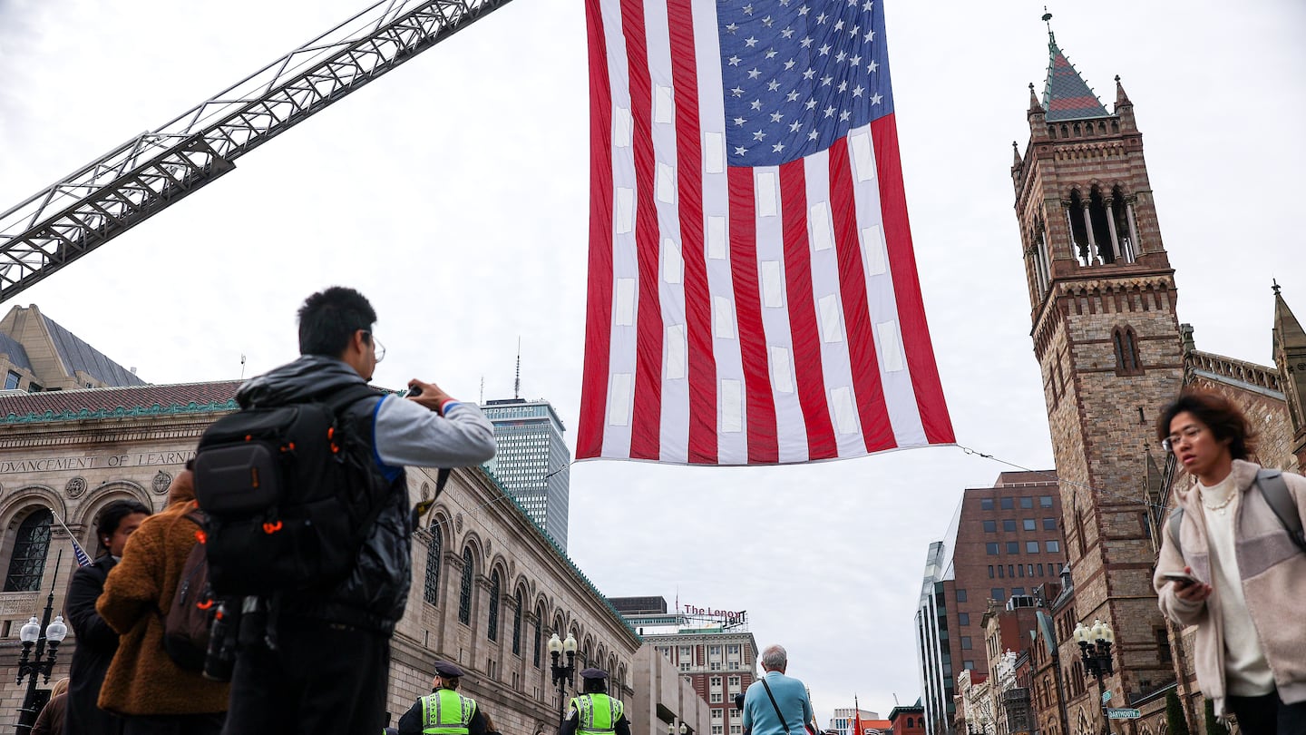 Spectators gather to photograph a large American flag hung at the start of the Veterans Day Parade on Boylston street in 2023.