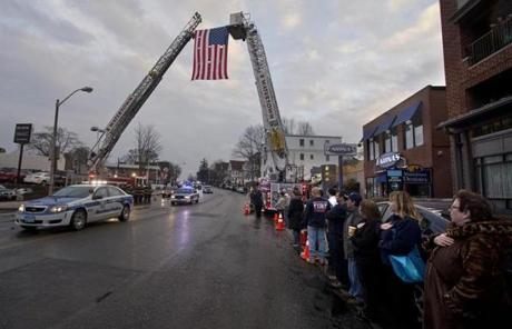 A procession carrying the body of Fire Lieutenant Edward Walsh Jr. passed under a flag held by Watertown ladder trucks.
