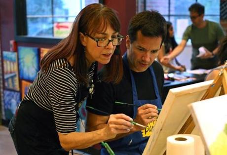 Longtime commercial artist Karin Samatis works with Eric Larson of Cambridge in a paint-and-sip class at Pinot?s Palette in Lexington.
