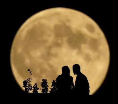 A couple sits on a bluff overlooking the Missouri River as the full moon rises Monday in Kansas City, Mo.
