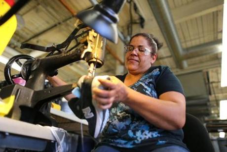 Eddy Maria Taveras used a hand-crank Singer sewing machine to make a repair on a running shoe at the New Balance factory in Lawrence.
