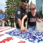 Boston Police Superintendent in Chief William Gross got assistance from Sandra Pacheco adding his print to the canvas. 