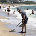 Don Mahoney, of Natick, worked his metal detector along Craigville Beach in Centerville while others hit the surf Monday.