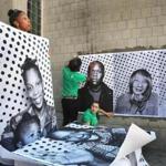 Aziza Robinson-Goodnight held up a giant xerox photo of herself and daughter August, 15 months, as volunteers pasted pictures of neighborhood residents on a wall outside the Boston Public Library in Roxbury.