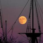 A near-full moon rose over the masts of the Mayflower II docked in Plymouth Harbor.