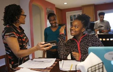 Boston, Massachusetts -- 11/25/2015- (L-R) Danita Brewster laughs as she pulls out a video of a choreographed routine her adopted daughters Ty-Janee, 12, and Que-Mya, 11, have to learn as her biological son, Arthur James Brewster III makes brownies in the kitchen at their home in Boston, Massachusetts November 25, 2015. Jessica Rinaldi/Globe Staff Topic: 26adoption Reporter: 
