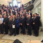 State and local officials gather for the unveiling of the bill at the State House.