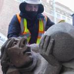 Matthew Lafond, Project Superintendent with Shawmut Design and Construction, brushes dirt off of a carved limestone grotesque.