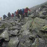 Teams carry Kathleen Maguire to the top of Mount Washington while facing low visibility.