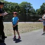 06/23/2016 -Brookline, MA- Brookline police officer Katie McCabe, left, gives a Òconehead citationsÓ to Daniel Leary (cq), while visiting Jean B. Waldstein Park with his babysitter Francisca Iturbe (cq) , right, in Brookline, MA on June 23, 2016. The Conehead Program offers free ice-cream to youths for practicing safe and responsible behavior. (Craig F. Walker/Globe Staff) section: Metro reporter: 