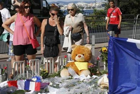 People react as they stand near tributes of flowers, flags and a stuffed toy two days after an attack by the driver of a heavy truck who ran into a crowd on Bastille Day killing scores and injuring as many on the Promenade des Anglais, in Nice, France, July 16, 2016. REUTERS/Pascal Rossignol 

