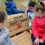 Olivia Craig, 7, right, on the Buddy Bench near the playground area at the Thomas W. Hamilton School in Weymouth. Children can sit on the bench when they feel left out and want a friend to play with. 
