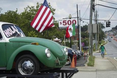 A pedestrian walked in front of a used car lot that is flying both the Mexican and American flags along Buford Highway in Norcross, Ga., late last month.
