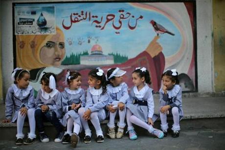 Palestinian schoolgirls sit in front of a mural on the first day of a new school year.
