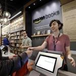Customer Kirsty Carey, left, gets ready to swipe her credit card for clerk Marissa Pacchiarotti, as she makes one of the first purchases at the opening day for Amazon Books, the first brick-and-mortar retail store for online retail giant Amazon, Tuesday, Nov. 3, 2015, in Seattle. The company says the Seattle store, coming two decades after it began selling books over the Internet, will be a physical extension of its website, combining the benefits of online and traditional book shopping. Prices at the store will be the same as books sold online. (AP Photo/Elaine Thompson)