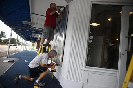 Pat Lena and Frank Capano (bottom) put up hurricane shutters as they prepared a Delray Beach shop for Hurricane Matthew. 
