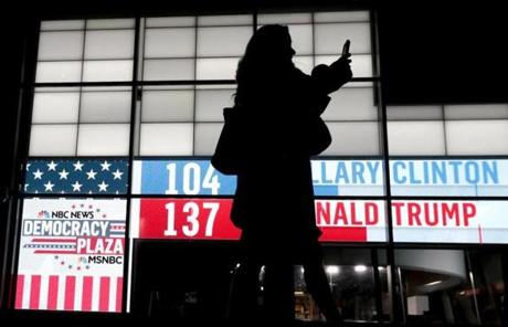A woman walks in front of a sign showing early Election Day results at Rockefeller Center, Tuesday, Nov. 8, 2016, in New York. (AP Photo/Julio Cortez)
