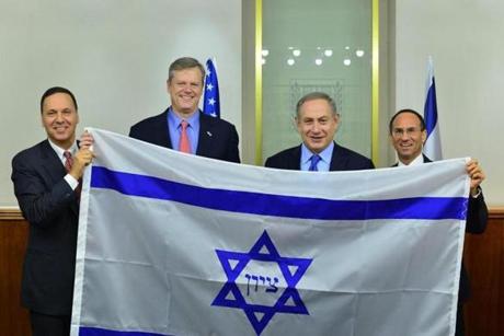 israelflag -(l to r) Brandeis President Ron Liebowitz, Massachusetts Gov. Charlie Baker, Israeli Prime Minister Benjamin Netanyahu and Consul General of Israel to New England Yehuda Yaakov hold a replica of an 1890s flag from Boston that, according to Brandeis research, influenced the design of today?s Israeli flag. Governor Charlie Baker met on Monday, December 12, with Israeli Prime Minister Benjamin Netanyahu to discuss the strong and unique relationship between Israel and Massachusetts. The meeting took place during the Baker-Polito Administration's Economic Development Mission to Israel. (Charlie Baker/Flickr)
