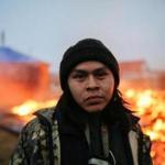 CANNON BALL, ND - FEBRUARY 22: O'Shea Spencer, 20, stands in front of the remains of a hogan structure. Campers set structures on fire in preparation of the Army Corp's 2pm deadline to leave the Oceti Sakowin protest camp on February 22, 2017 in Cannon Ball, North Dakota. Activists and protesters have occupied the Standing Rock Sioux reservation for months in opposotion to the completion of the Dakota Access Pipeline. (Photo by Stephen Yang/Getty Images)
