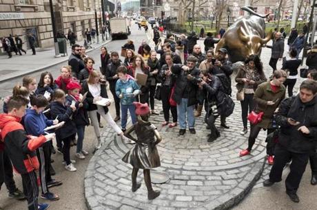 A crowd gathers around a statue of a fearless girl facing the Wall Street Bull, Wednesday, March 8, 2017, in New York. The statue was installed by an investment firm in honor of International Women's Day. An inscription at the base reads, 