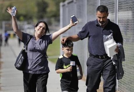 Adrian Velasco, a 7-year-old student at North Park Elementary School, walks with his father, Hector, as Velasco's mother, Raquel, raises her hands in relief after they were reunited at Cajon High School, Monday, April 10, 2017, in San Bernardino, Calif., after a deadly shooting occurred at the elementary school. (AP Photo/Jae C. Hong)
