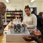 Boston, MA- May 05, 2017: Ted Landsmark, left, talks with Ashanti Dabneysmall, 15, about her memorial design while visiting John W Mccormack middle school in Dorchester, MA on May 05, 2017. The 8th-grade civics class ended their studies of segregation by creating memorials dedicated to racial issues. Ted Landsmark appeared in a Pulitzer Prize winning photograph by Stanley Forman, being assaulted by a man using an American flag on a pole in 1976, during a protest against the desegregation busing.(Craig F. Walker/Globe Staff) section: metro reporter: 