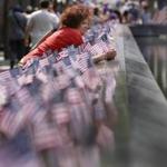 A woman paused among American flags that were inserted in each of the 2.983 names on the borders of the reflecting pools of the 9/11 Memorial. 