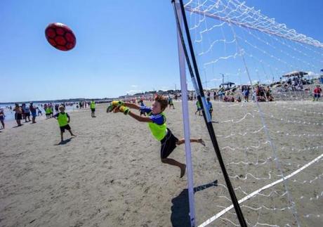 Ball and goalie are airbourne at the Boston Beach Soccer Tournament Series at Nantasket Beach.
