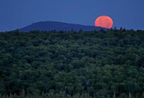 The full moon sat behind Hunt Mountain on a privately owned tract of land surrounded by land that now comprises the Katahdin Woods and Waters National Monument near Patten, Maine.
