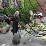 A woman with her luggage rolled past wires, cut trees, and debris Thursday.