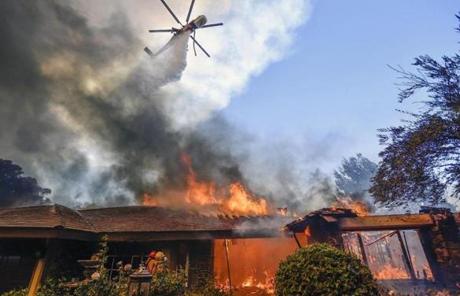 WILDFIRES SLIDER A helicopter dumps water on a home as firefighters battle a wildfire in Anaheim Hills in Anaheim, Calif., Monday, Oct. 9, 2017. Wildfires whipped by powerful winds swept through Northern California sending residents on a headlong flight to safety through smoke and flames as homes burned. (Jeff Gritchen/The Orange County Register via AP)
