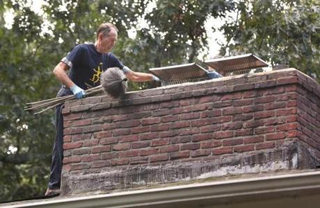 Carlisle, MA - 10/5/2017 - With his 25-year-old son Jacob Liverman (cq) (partly hidden), chimney sweep Erwin Liverman (cq), 71, cleans three chimney flues on a Carlisle home. From the age of 8, the elder sweep learned the business from his father, Abraham Liverman (cq). His own son helped him from the age of 8 or 9. 