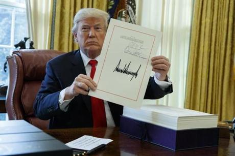 President Donald Trump shows off the tax bill after signing it in the Oval Office of the White House, Friday, Dec. 22, 2017, in Washington.
