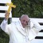 Pope Francis loses his skull cap, as he holds up a cross that reads in Spanish 