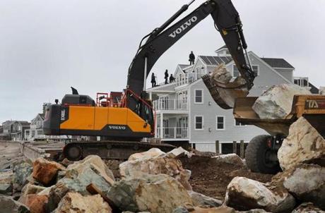 Workers rushed to rebuild a breached seawall in the Brant Rock section of Marshfield that was damaged by the last Nor'easter. Roofers repaired a roof on one of the oceanfront homes in the background.
