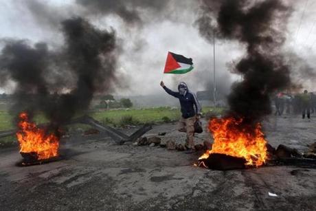 A Palestinian protester wavec the Palestine flag during clashes marking Land Day in the West Bank City of Ramallah. 
