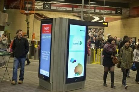 Commuters walked past a digital advertising and information screen at the Harvard Square MBTA station. 
