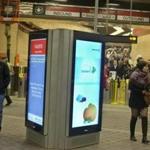 Commuters walked past a digital advertising and information screen at the Harvard Square MBTA station. 