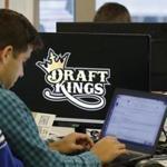 FILE - In this Sept. 9, 2015, file photo, Bear Duker, a marketing manager for strategic partnerships at DraftKings, works at his computer at the company headquarters in Boston. Daily fantasy sports rivals DraftKings and FanDuel have agreed to merge after months of speculation and increasing regulatory scrutiny. The two companies made the announcement Friday, Nov. 18, 2016, saying the combined organization would be able to reduce costs as they work to become profitable and battle with regulators across the country to remain legal. (AP Photo/Stephan Savoia, File)