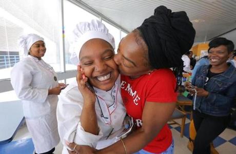 As she talks to her father on the phone, 18-year-old Taya Henderson is kissed by her mother, Ebony. Autasia Fuentes (left) was Henderson?s Madison Park High School tteammate, and they prepared a winning meal in a cooking contest.
