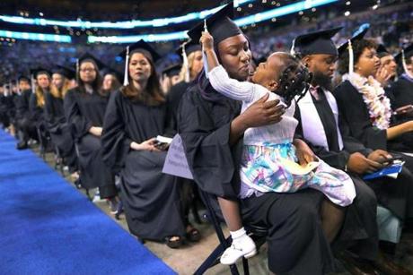 Angelania Vil, 3, sits on her mother Nastassia?s lap and plays with her tassel as she waits for her early-education degree from Mass Boston during commencement at TD Garden.
