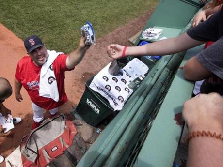 Craig Bjornson, the Red Sox bullpen coach, gives sunflower seeds to bleacher fans before a game. 
