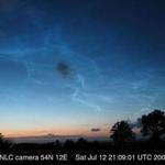 Noctilucent clouds in Wismar, Germany. they appear blue at higher elevations and become white at lower elevations. The black spots in the center and lower right corner are regular, tropospheric clouds. 