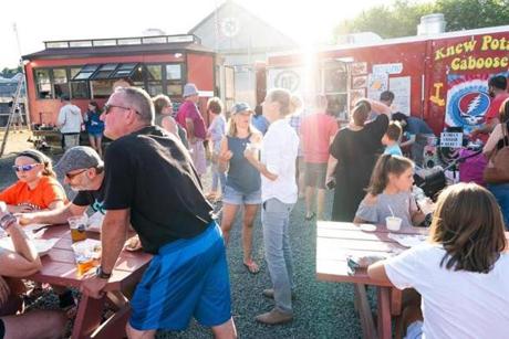 The scene at Congdon?s After Dark Food Truck Park includes people sitting at tables and walking among the trucks
