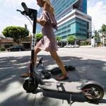 A pedestrian walks between two Bird dockless scooters in Los Angeles.