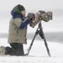 04byrne -- MassWildlife photographer Bill Byrne hunkers behind his Nikon 400mm f2.8 lens during a blizzard on a Nantucket Beach. He was photographing Long-tailed ducks in the surf, as some of the drakes had courtship on their minds. (Mark Wilson)
