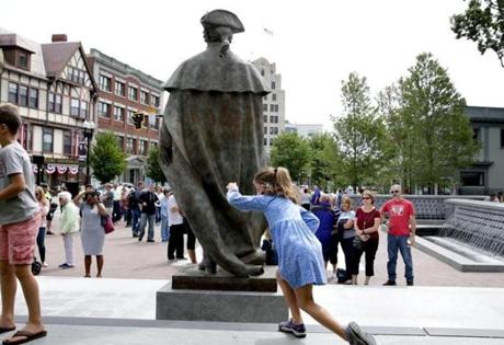 A young girl played behind the newly unveiled statue of John Hancock in Quincy on Saturday.
